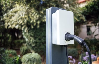 Electric vehicle charging station features a black charging cable in a vibrant garden, highlighting the integration of technology and nature for sustainable energy use